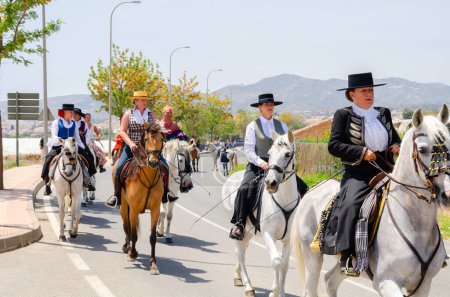 Photo for NERJA, SPAIN - 15 MAY 2022 Women in flamenco dresses and men on Andalusian horses dressed in their best traditional folk costumes and wide-brimmed hats taking part in the festival parade - Royalty Free Image
