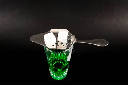 Vodka verde aromatizado llamado Absenta servido en un vaso de chupito con una cuchara especial con cubitos de azúcar blanco