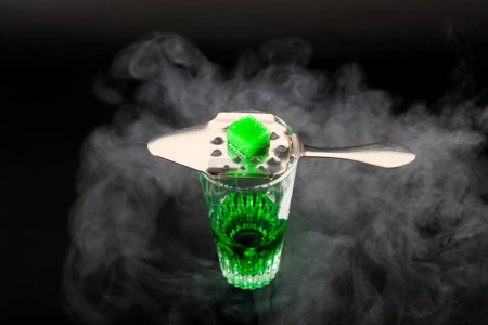 Foto de Vodka verde aromatizado llamado Absenta servido en un vaso de chupito con una cuchara especial con cubitos de azúcar blanco - Imagen libre de derechos