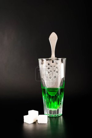 Vodka verde aromatizado llamado Absenta servido en un vaso de chupito con una cuchara especial con cubitos de azúcar blanco