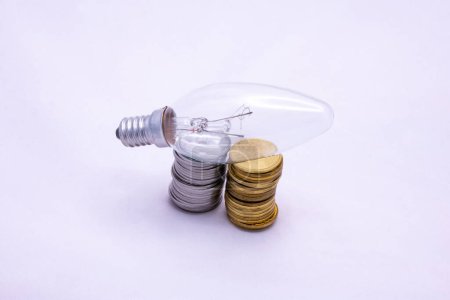 Photo for A photograph with coins and an incandescent lamp illustrates the system of taxes and fees associated with the electricity system. Photo for use in advertisements, presentations. - Royalty Free Image