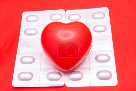 Téléchargez les photos : Figure of heart lies on two blisters with drugs in pills on red background. Conceptual photo for treatment methods and groups of drugs for treatment of diseases of the heart and cardiovascular system - en image libre de droit