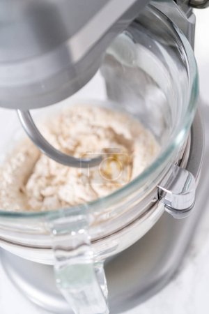 Mixing ingredients in a large glass mixing bowl to pizza dough.