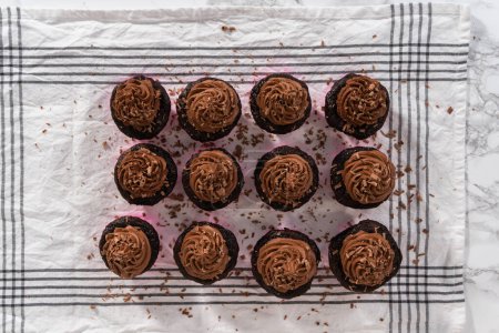 Téléchargez les photos : Pose plate. Piping chocolat ganache glaçage sur le dessus de cupcakes au chocolat. - en image libre de droit