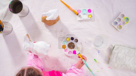 Photo for Flat lay. Little girl painting paper mache figurine at homeschooling art class. - Royalty Free Image