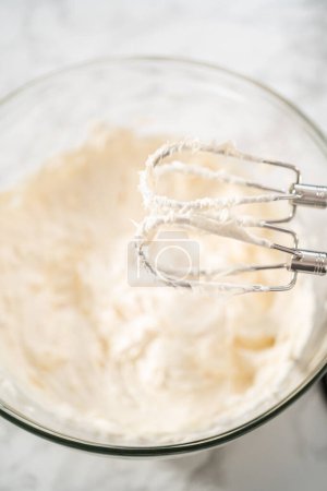 Foto de Batiendo crema de mantequilla glaseado en un tazón de vidrio con una batidora eléctrica para preparar el glaseado de crema de mantequilla de menta. - Imagen libre de derechos