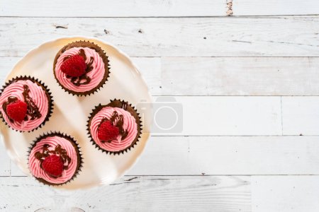 Foto de Acostado. Cupcakes de frambuesa de chocolate gourmet rociado con ganache de chocolate y cubierto con una frambuesa fresca. - Imagen libre de derechos
