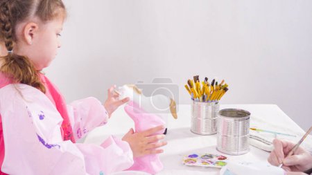 Photo for Little girl painting paper mache figurines with acrylic paint for her homeschooling art project. - Royalty Free Image