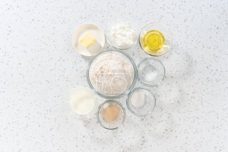 Photo for Flat lay. Measured ingredients in glass mixing bowls to bake naan dippers. - Royalty Free Image