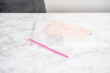 Foto de Triturar caramelos de menta en una bolsa de plástico con un rodillo de mármol en una tabla de cortar blanca. - Imagen libre de derechos