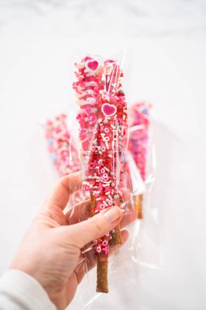 Téléchargez les photos : Baguettes de bretzel recouvertes de chocolat décorées de saupoudres en forme de cœur pour la Saint-Valentin emballées dans un sac transparent. - en image libre de droit