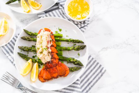 Sering garlic lobster tails with steamed asparagus and lemon wedges on a white plate.