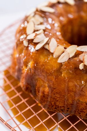 Photo for Glazing homemade caramel glaze over freshly baked apple bundt cake and garnishing with sliced almonds. - Royalty Free Image