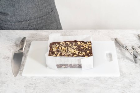 Foto de Extracción de caramelo de avellana de chocolate de una sartén cuadrada de pastel de queso forrada con pergamino. - Imagen libre de derechos