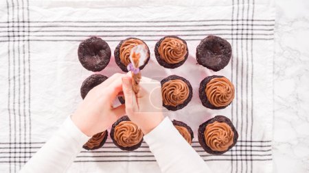 Téléchargez les photos : Pose plate. Pas à pas. Piping chocolat ganache glaçage sur le dessus de cupcakes au chocolat. - en image libre de droit