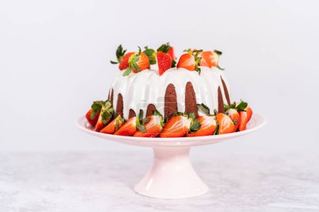 Photo for Fresh strawberries..Red velvet bundt cake with cream cheese frosting garnished with fresh strawberries on a pink cake stand for Valentines Day. - Royalty Free Image