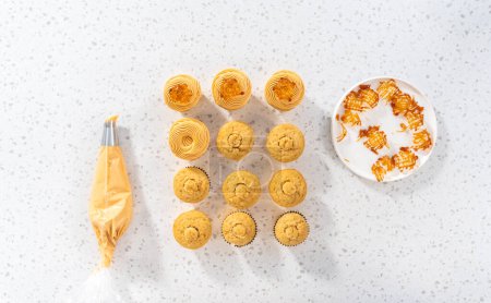 Photo for Flat lay. Piping dulce de leche buttercream frosting over vanilla cupcakes filled with caramel. - Royalty Free Image