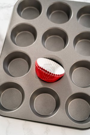 Foto de Recoger masa de pastel con cuchara de masa en forros de papel de magdalena para hornear pasteles de menta de chocolate. - Imagen libre de derechos