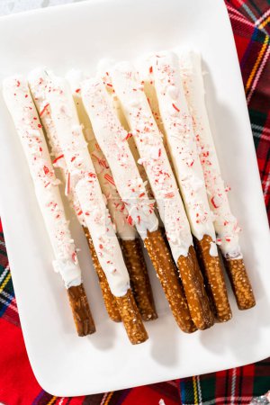 Pile of homemade candy cane chocolate-covered pretzel rods on a white serving plate.