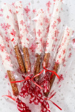 Packaging homemade candy cane chocolate-covered pretzel rods into clear plastic bags for Christmas gifts.