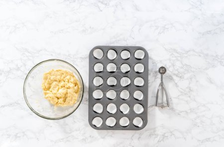 Foto de Flat lay. Scooping cupcake batter with dough scoop into a baking cupcake pan with liners to bake mini vanilla cupcakes with ombre pink buttercream frosting. - Imagen libre de derechos