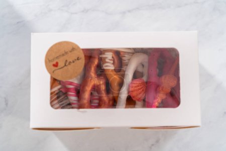 Foto de Embalaje gourmet chocolate cubierto torceduras pretzel en una caja de regalo de papel blanco lleno de trozos de papel. - Imagen libre de derechos