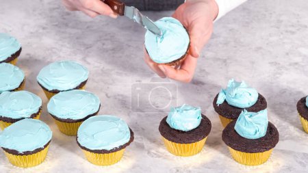 Foto de Paso a paso. Recoger glaseado de crema de mantequilla azul en la parte superior de los cupcakes de chocolate. - Imagen libre de derechos