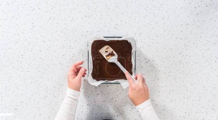 Photo for Flat lay. Pouring fudge mixture into the baking pan lined with parchment paper to prepare chocolate fudge with peanut butter swirl. - Royalty Free Image