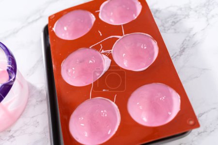 Foto de Rellenar moldes de chocolate de silicona con chocolate rosa derretido para preparar bombas de chocolate caliente. - Imagen libre de derechos