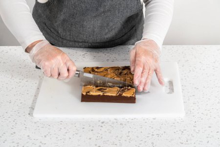 Téléchargez les photos : Couper le caramel au chocolat avec du beurre d'arachide en petits morceaux sur une planche à découper blanche. - en image libre de droit