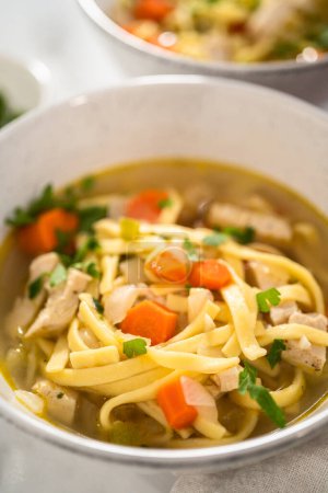 Photo for Serving chicken noodle soup with kluski noodles in white ceramic soup bowls. - Royalty Free Image