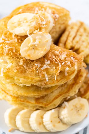 Photo for Eating freshly baked coconut banana pancakes garnished with sliced bananas and toasted coconut. - Royalty Free Image