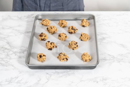 Photo for Scooping cookie dough with dough scoop into a baking sheet lined with parchment paper to bake soft oatmeal raisin walnut cookies. - Royalty Free Image