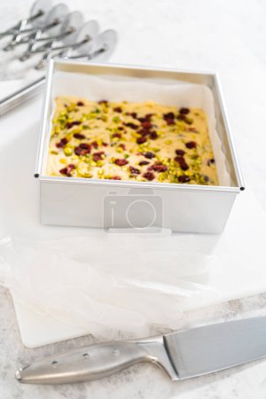 Foto de Extracción de caramelo de pistacho de arándano de una sartén cuadrada de pastel de queso forrada con pergamino. - Imagen libre de derechos