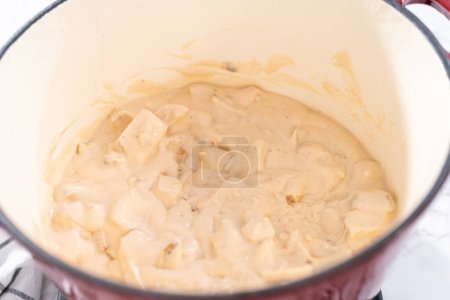 Téléchargez les photos : Mélanger les ingrédients dans un four hollandais émaillé pour préparer des pâtes au poulet alfredo. - en image libre de droit