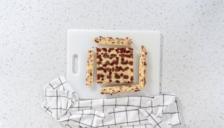 Photo for Flat lay. Cutting white chocolate cranberry pecan fudge into small pieces on a white cutting board. - Royalty Free Image