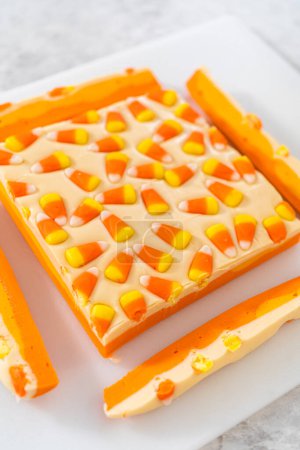 Téléchargez les photos : Découpe de caramel au maïs en morceaux carrés sur une planche à découper blanche. - en image libre de droit