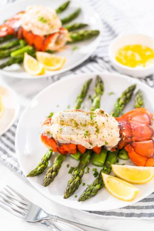 Photo for Sering garlic lobster tails with steamed asparagus and lemon wedges on a white plate. - Royalty Free Image