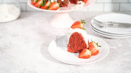 Téléchargez les photos : Pas à pas. Tranche de gâteau bundt en velours rouge avec glaçage au fromage à la crème garnie de fraises fraîches sur une assiette blanche. - en image libre de droit