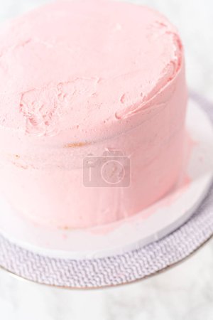 Photo for Covering mermaid-themed 3 layer vanilla cake with a crumb coat. - Royalty Free Image