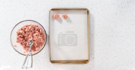 Téléchargez les photos : Pose plate. Ramasser la viande hachée avec une pelle à pâte dans une plaque à pâtisserie tapissée de papier parchemin pour préparer des boulettes de viande cuites au four. - en image libre de droit