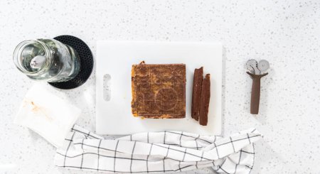 Foto de Acostado. Cortar la mantequilla de cacahuete de chocolate en trozos pequeños en una tabla de cortar blanca. - Imagen libre de derechos