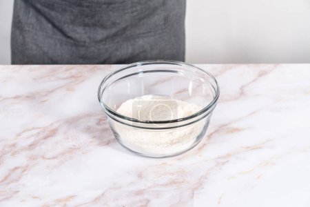 Téléchargez les photos : Mélanger les ingrédients dans un grand bol à mélanger en verre pour cuire le muffin sharlotka aux pommes. - en image libre de droit