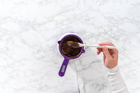 Téléchargez les photos : Pose plate. Fondre des pépites de chocolat dans un melting pot de bonbons pour faire du glaçage au chocolat pour biscuits sablés en forme de panda. - en image libre de droit