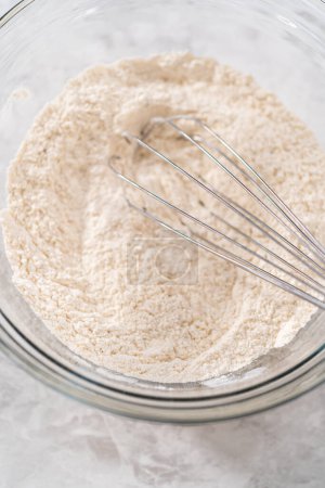 Foto de Mezclar ingredientes secos con un batidor de mano en un tazón grande para hornear pastel de zanahoria con glaseado de queso crema. - Imagen libre de derechos