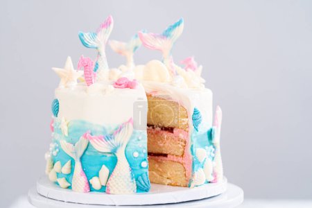 Slicing mermaid-themed 3 layer vanilla cake on a cake stand.