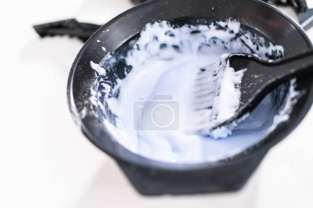 Téléchargez les photos : Mélange de teinture de couleur de cheveux dans un bol de mélange noir avec un pinceau. - en image libre de droit