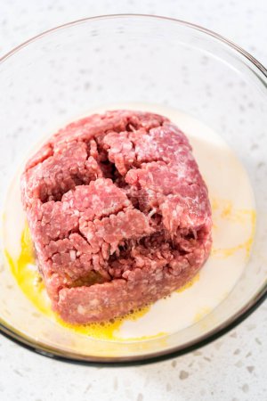 Téléchargez les photos : Mélanger les ingrédients avec une purée de pommes de terre dans un bol de mélange en verre pour préparer des boulettes de viande cuites au four. - en image libre de droit