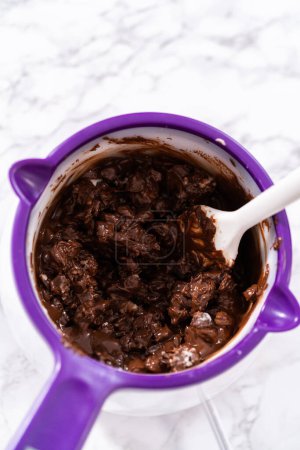 Téléchargez les photos : Fondre des pépites de chocolat dans un melting pot de bonbons pour préparer des fraises recouvertes de chocolat. - en image libre de droit