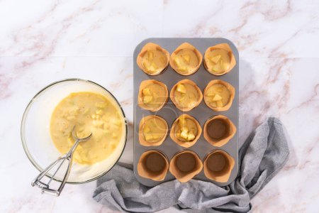 Téléchargez les photos : Pose plate. Ramasser la pâte dans la casserole à cupcake doublée de doublures de muffins en parchemin pour cuire des muffins sharlotka. - en image libre de droit